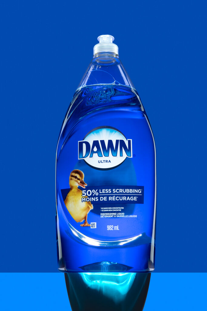 Bouteille transparente de liquide vaisselle Dawn avec illustration de caneton sur fond bleu vif