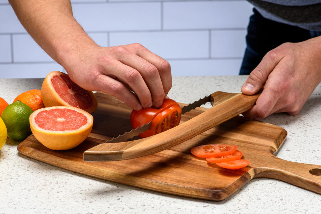 Couteau à pain tranchant une tomate sur une planche avec des pamplemousses et agrumes à proximité
