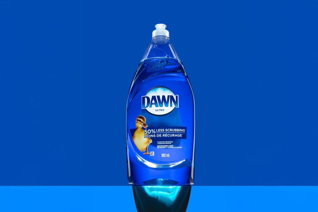 Bouteille transparente de liquide vaisselle Dawn avec illustration de caneton sur fond bleu vif
