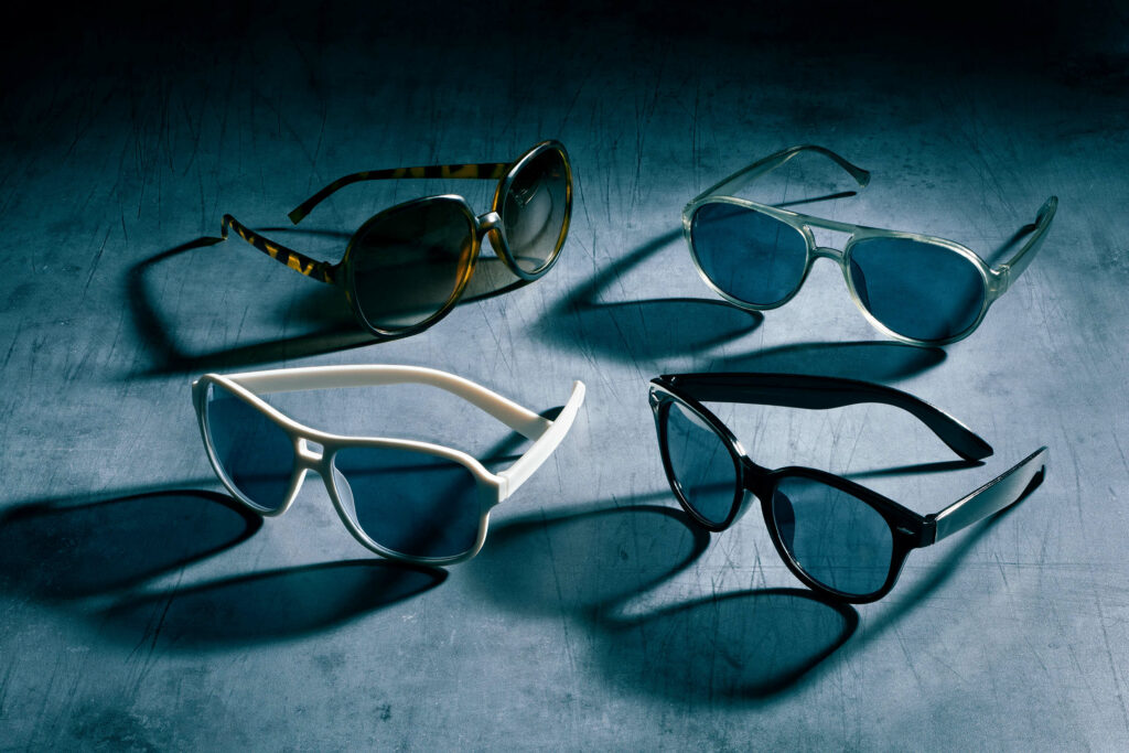 Photo en studio de quatre lunettes de soleil variées avec ombres marquées sur fond bleu texturé